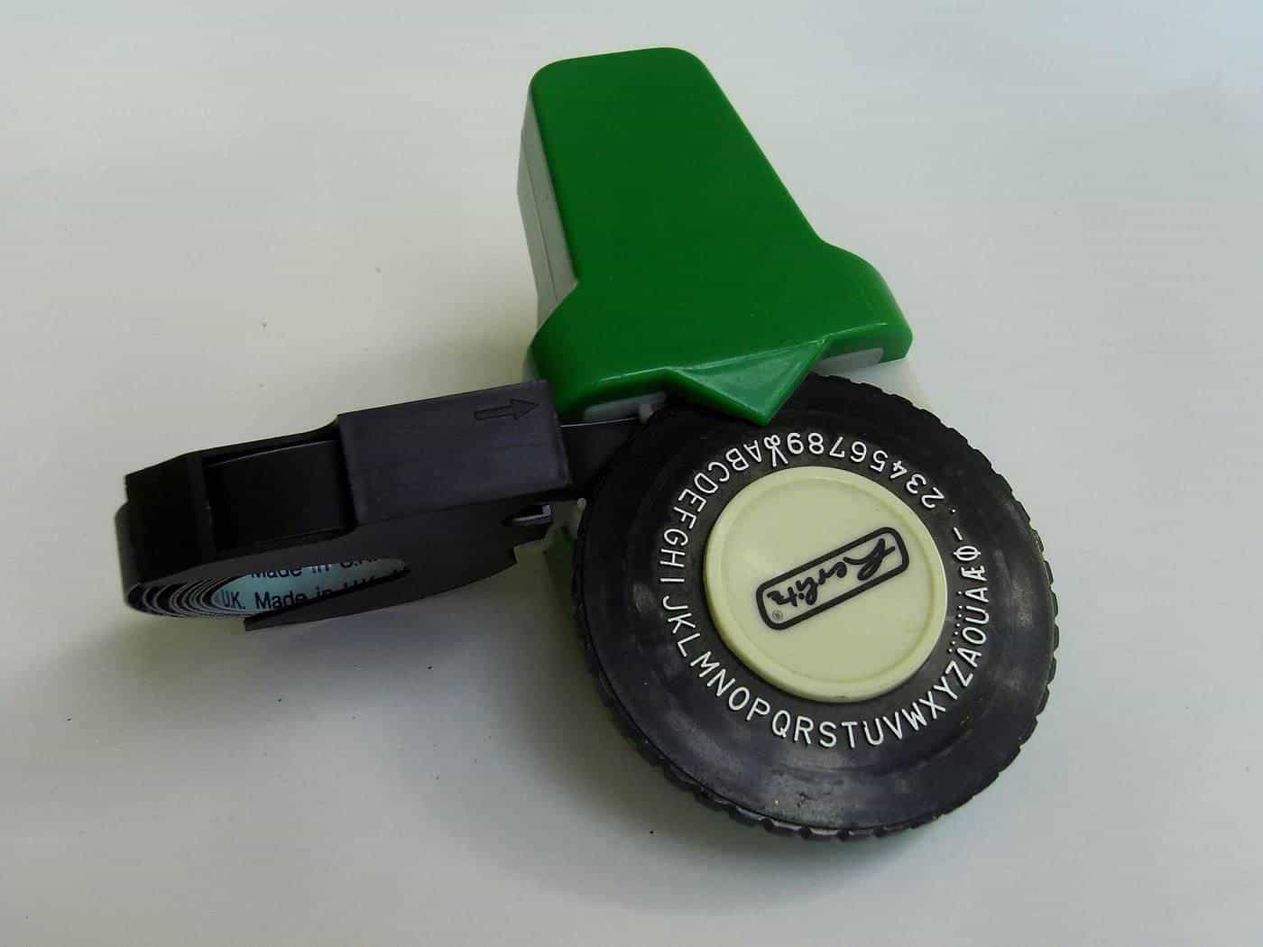 A handheld embossing label maker with a wheel of letters and a strip of label tape