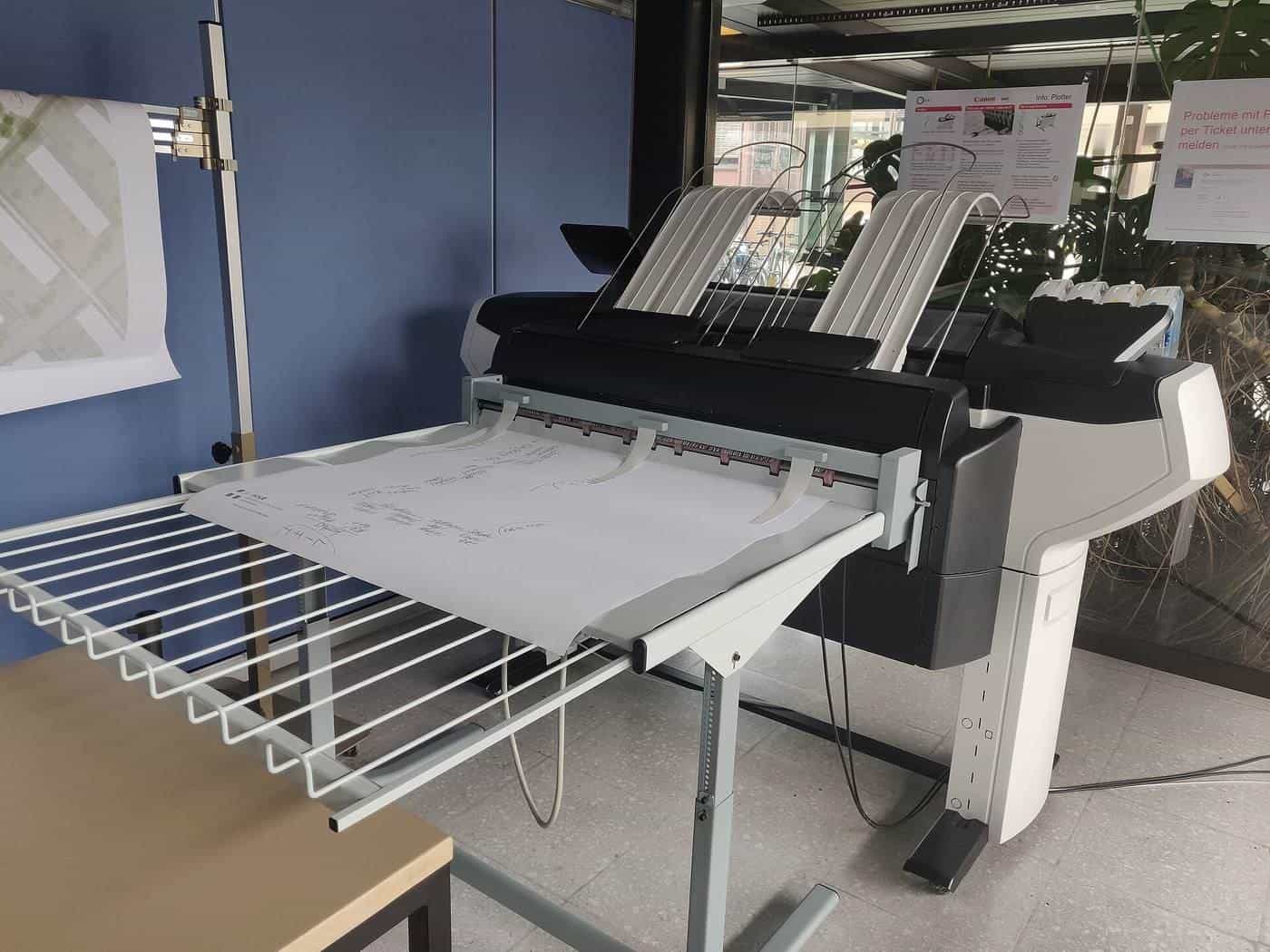A large-format printer with paper output trays in a print room