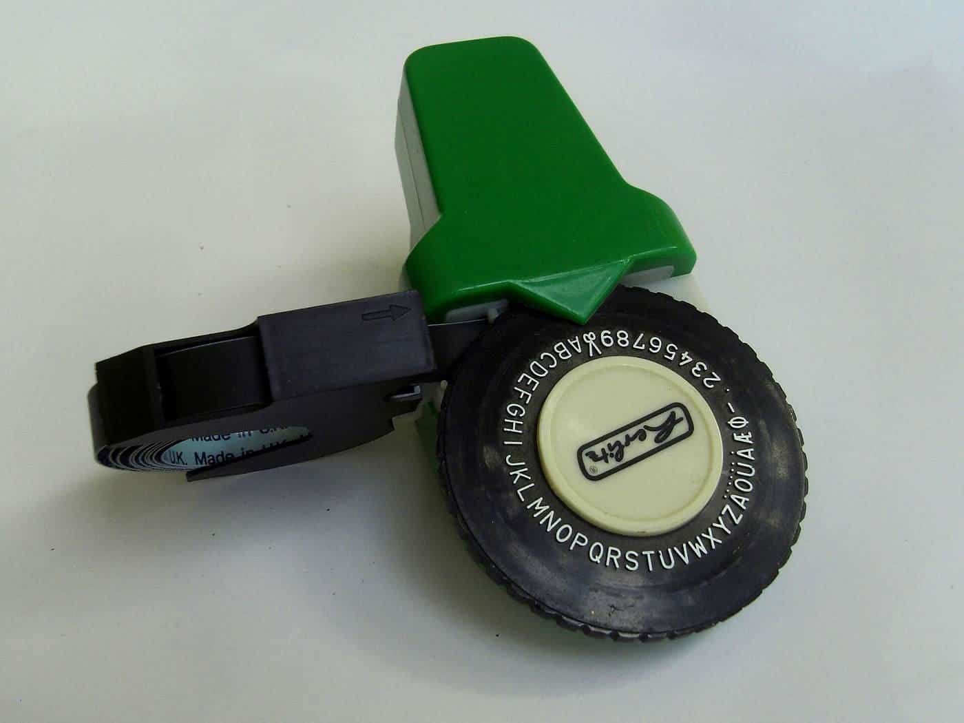 A handheld embossing label maker with a wheel of letters and a strip of label tape