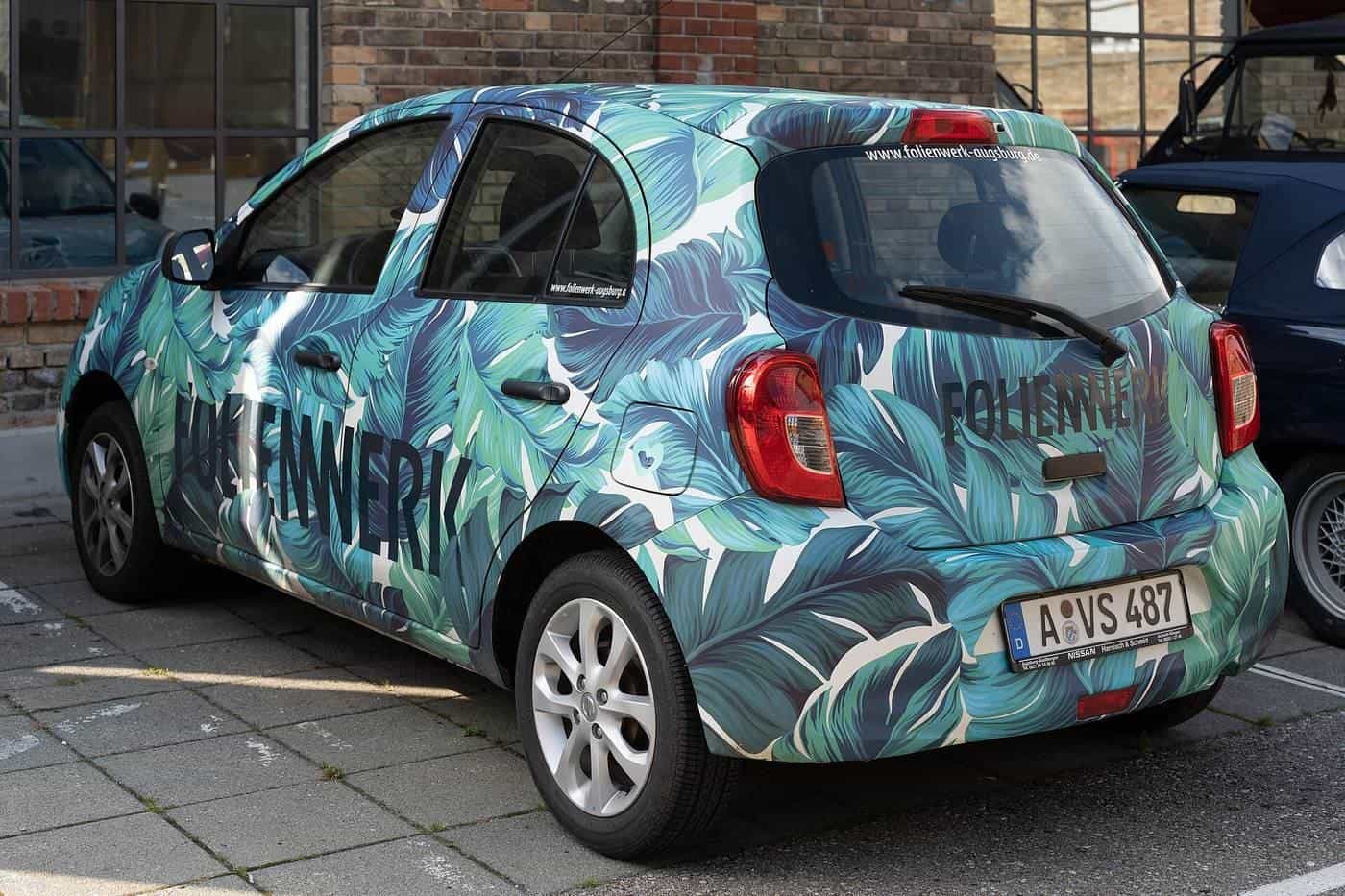 A hatchback covered in a leafy patterned vinyl wrap parked on a city street