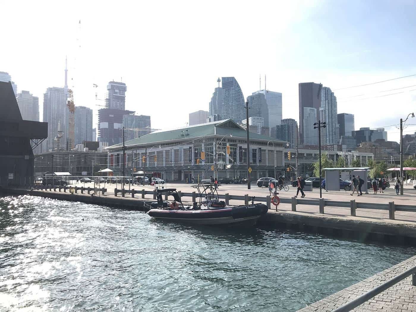 A small motor boat on a city harbour with tall buildings and a ferry terminal in the background