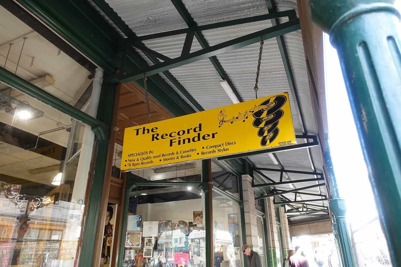 A bright yellow hanging shop sign under a verandah on a Fremantle street